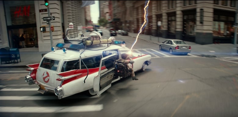 A figure sits on a jump seat protruding from the side of a car speeding through an intersection. The figure is holding a gun that shoots an electrical bolt. 