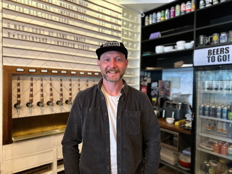 a man stands in causal clothing in front of a beer menu and line of taps. 