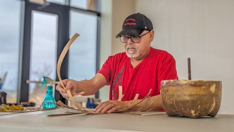 A man in a red Tshirt weaving together pieces of wood 