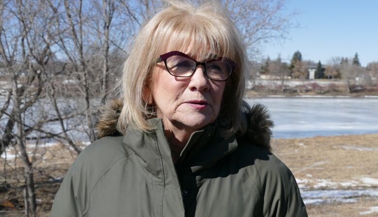 A woman wearing a winter jacket is pictured standing near a frozen river.