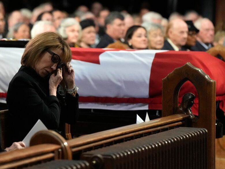 A woman wipes away tears, with a casket wrapped in a Canadian flag in the background.