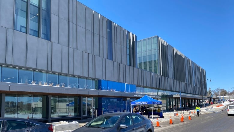 On a sunny day, a large building is shown next to a parking lot