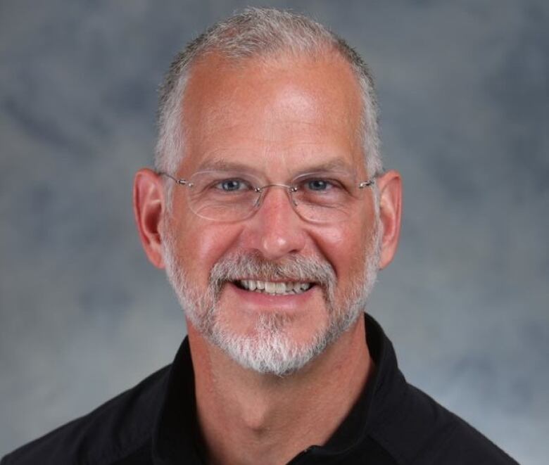 A man with glasses and salt and pepper hair smiles at the camera.