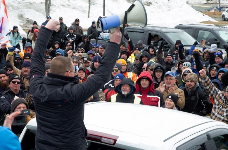 A man in the back of a pickup truck with his arms raised in the air, as people stand in front of him and cheer.