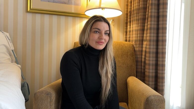 A woman sits in a chair in a hotel room.