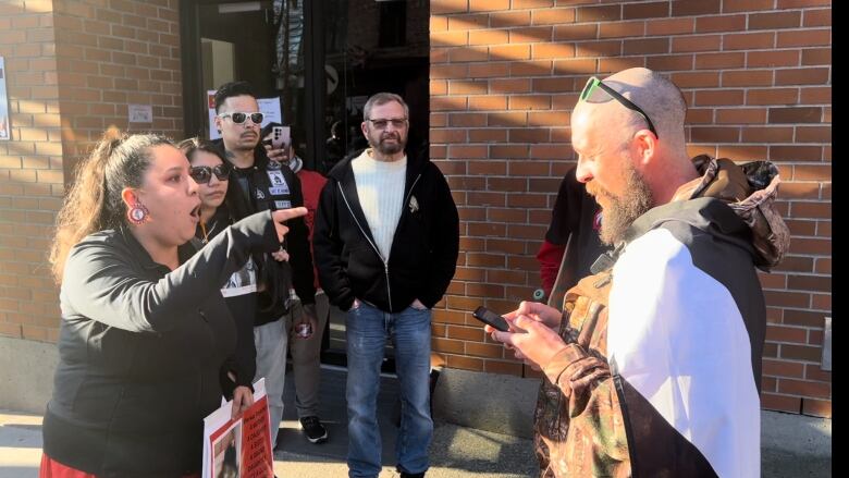 A woman points her finger at a man who is looking at his phone