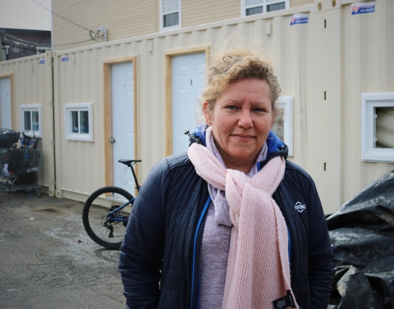 A woman in a pink scarf and a blue Irving jacket stands in front of modified shipping containers. 