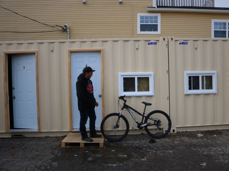 A man stands in front of a shipping container with a bicycle. 