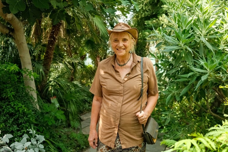 A person in safari clothes holds a purse amid tropical surroundings.