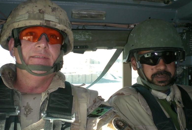 Two men wearing helmets and military uniforms sit inside a military patrol vehicle