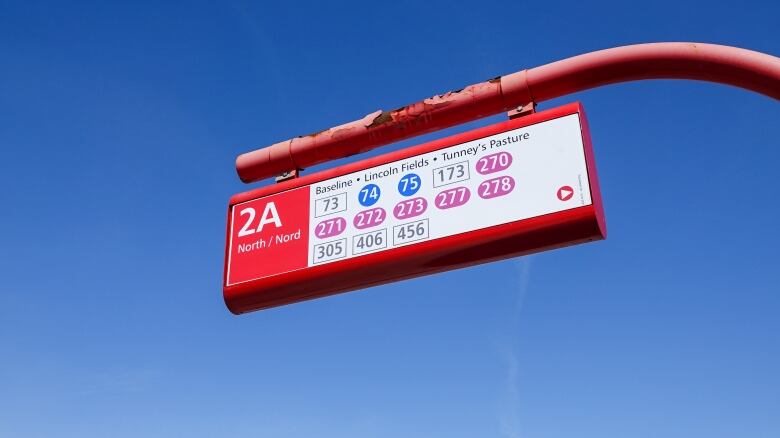 A bus stop sign with 13 route numbers. They're colour-coded a few different ways.