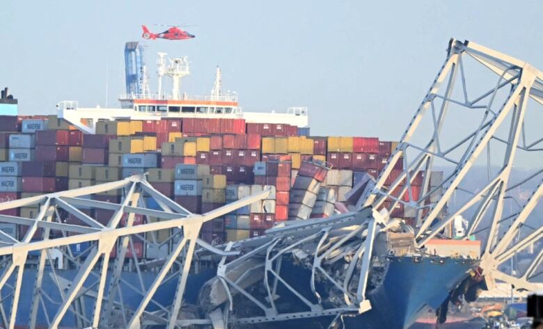 The collapsed steel frame of a bridge rests on top of a container ship that hit the structure.