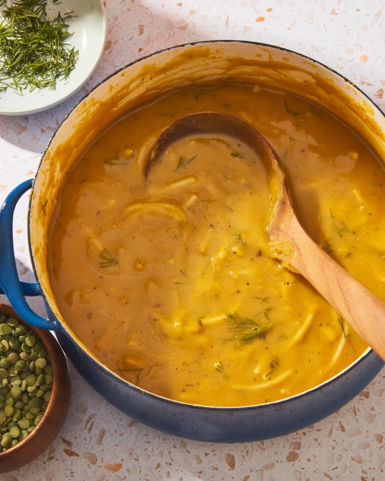 Overhead shot of a blue pot of yellow soup with a wooden ladle in it. It's sitting on a counter. 