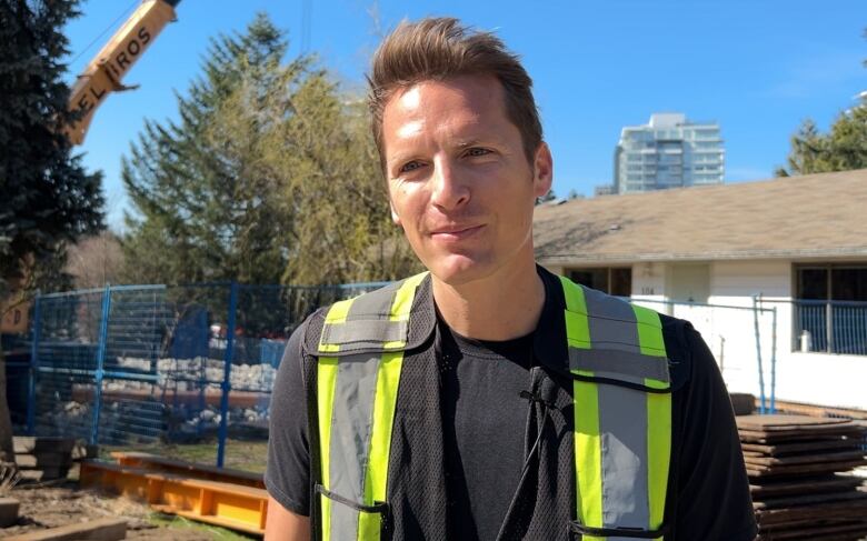 A man in a construction vest stand outside a house with construction equiptment around it. 