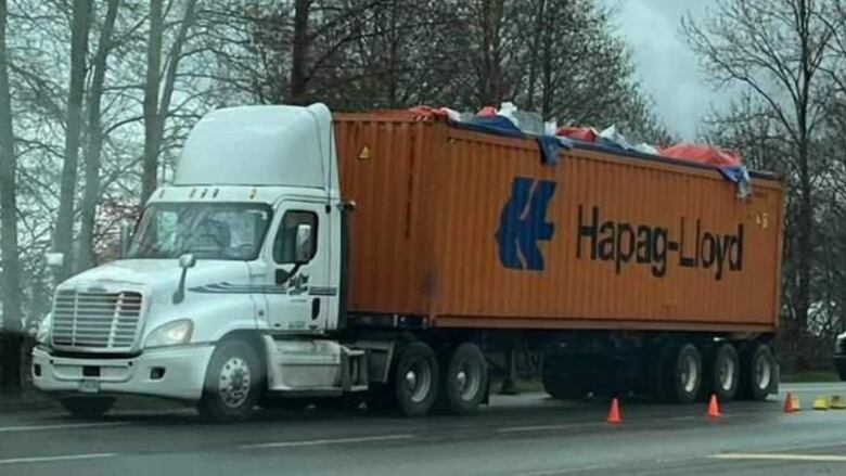 A white trailer truck carrying an orange container is seen parked on the side of a highway