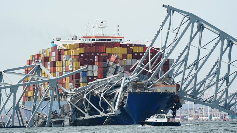 A cargo ship sits under a collapsed bridge