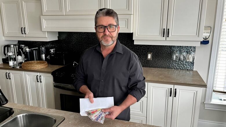 A man stands in his kitchen holding an envelope with flyer clippings. 