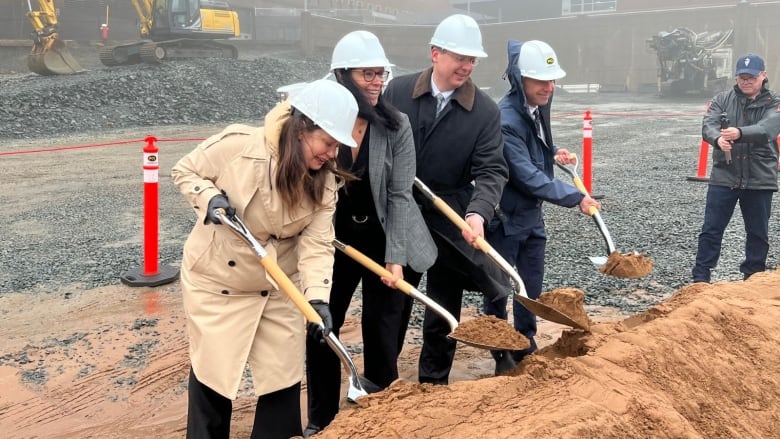 Four people shovel dirt in a construction site on a foggy day.