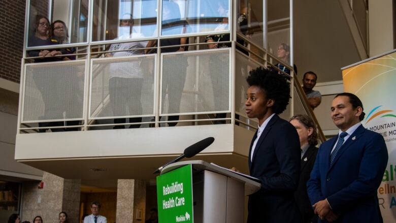 A person stands at a podium as people fill a staircase listening.