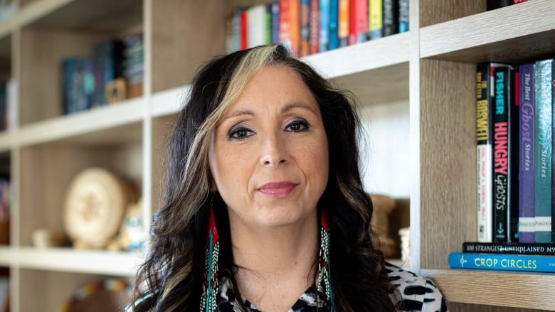 A woman poses for a portrait in front of a bookshelf.