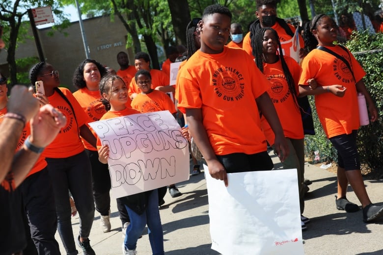 Several children in the same coloured tshirts hold signs and walk during a demonstration.