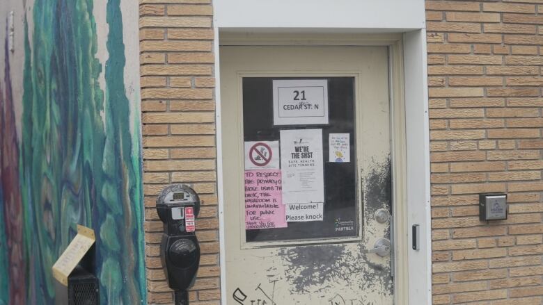 A door on a brick building with different signs posted indicating supervised consumption services are available inside.