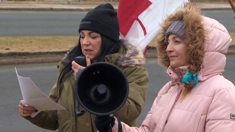 A woman in a green jacket speaks into a megaphone, standing beside a woman in a pink jacket.