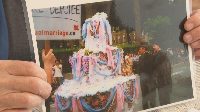 a man holding up a photo of a giant pink cake