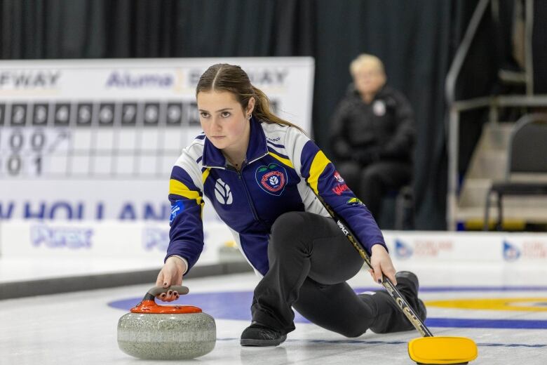 A woman kneels above ice throwing a curling stone.