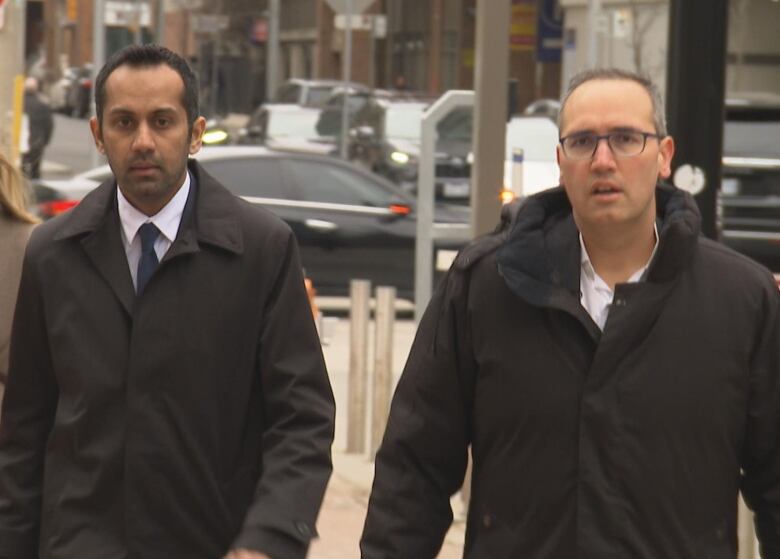 Two men in coats walking on sidewalk.