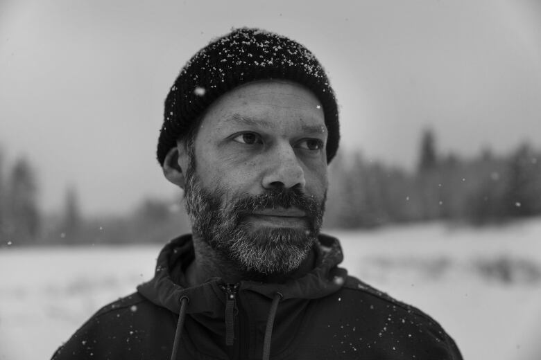 A black and white portrait of a white man wearing a tuque and a beard in a snowy landscape.