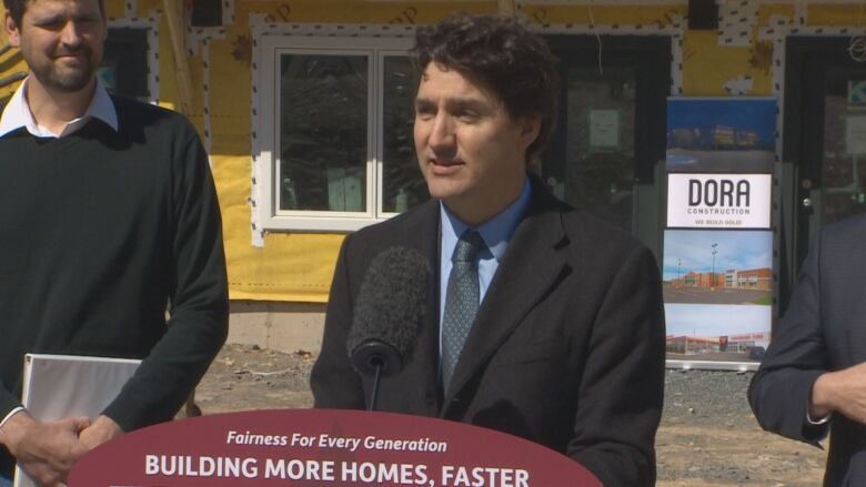 Man in a suit stands in front of a home that's under construction.