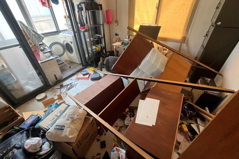 Large wooden pieces of furniture are shown strewn on the floor, along with other debris, in a compact apartment.