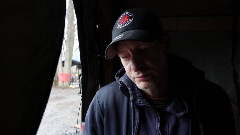 A profile of a man sitting half in the dark. Light comes in through an open tent flap. He's looking down with a sad expression on his face.