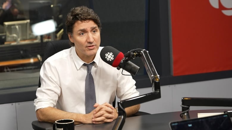 A man sits at a desk with a microphone in front of him. 