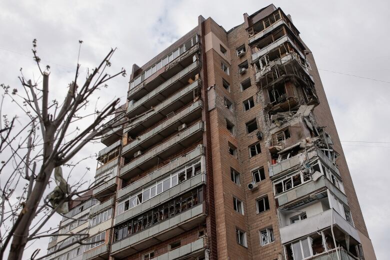 A multistorey residential building is shown, with extensive damage to balconies and units shown, especially in one corner of the building.