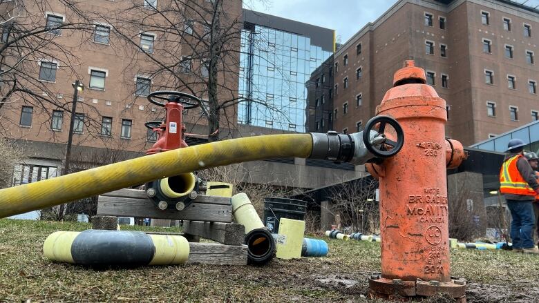 A fire hydrant with a yellow hose is shown next to a brick building.