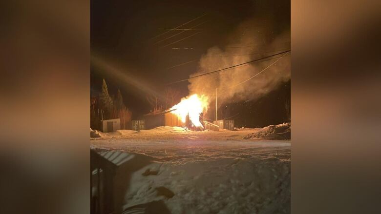 A fire is seen at a structure in the night, surrounded by snow and smoke.