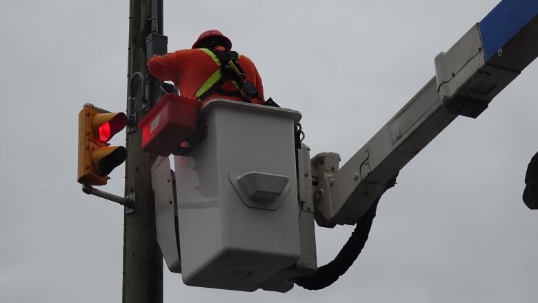 A man in high-visibility orange clothes and a hard hat works on a traffic light that's glowing red.