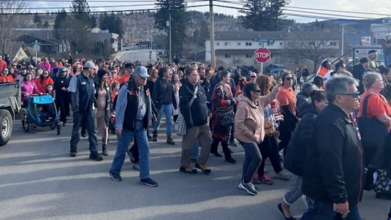 A large crowd of people walks down a city street on their way to Quesnel city hall. 