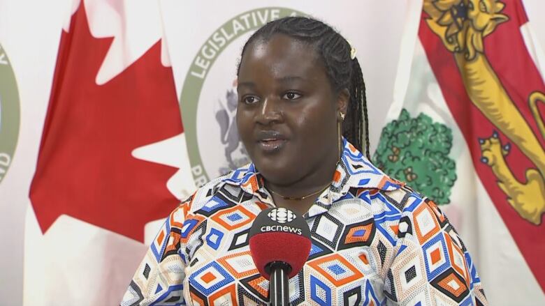 A woman in a colourful shirt speaks into a microphone in front of a PEI flag.