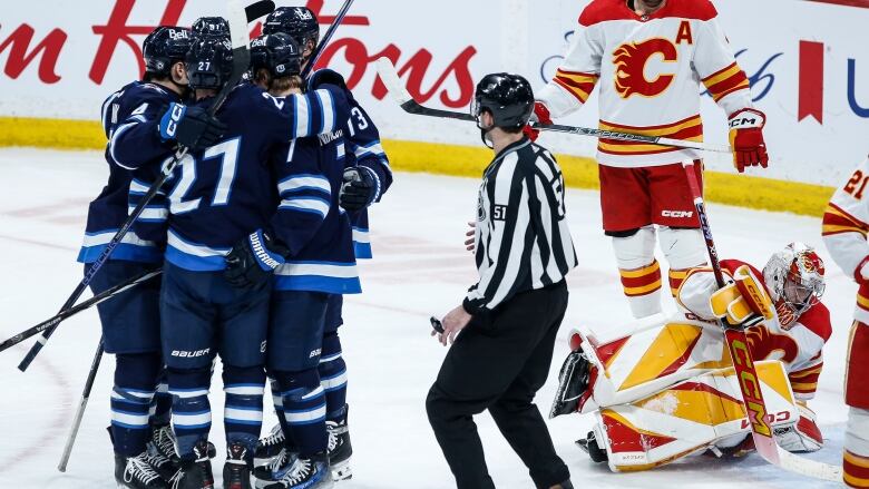 Five Jets players hug in celebration while Calgary's goaltender gets up off the ice.