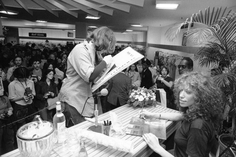 A women with long brown curly hair signs autographs at a record store in New York City in a 1978 photo.