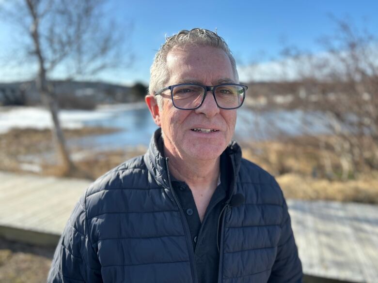 A head-and-shoulders shot of a man wearing glasses, standing outside on a clear day.