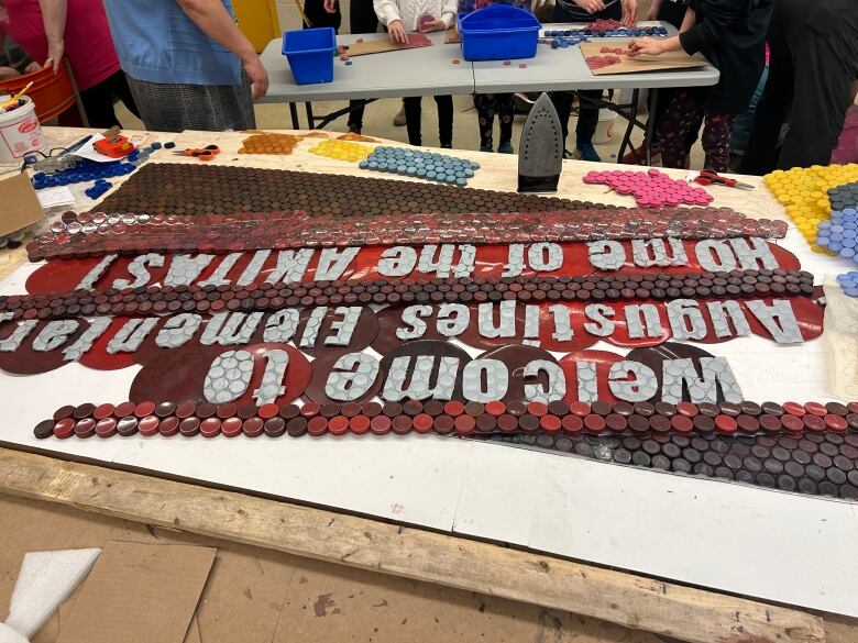 A panel of bottle caps, ironed flat, says 'Welcome to Augustine's Elementary, Home of the Akitas.'