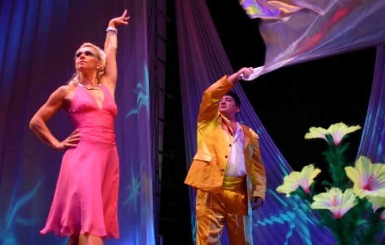 A man in a yellow suit waves a flag over a woman posing in a pink dress.