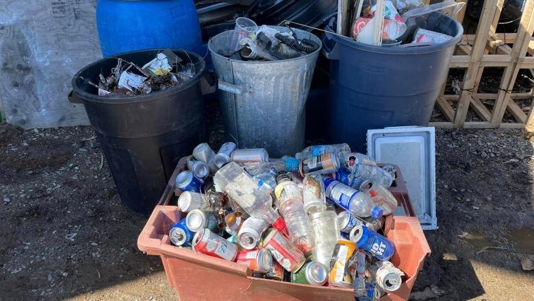 Three garbage cans full of trash and a bin of bottles.