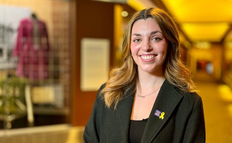 A woman wearing a black coat with a small yellow ribbon and a pin with the words 'Bring them home.'