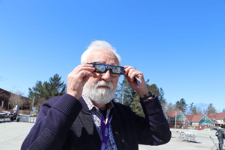 Man with white hair adjusts eclipse glasses over his spectacles.