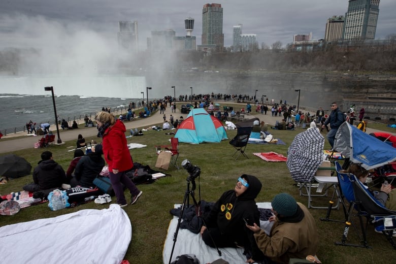 A crowd of people setting up on a patch of grassy area at Niagara Falls on the American side, to watch the total solar eclipse.